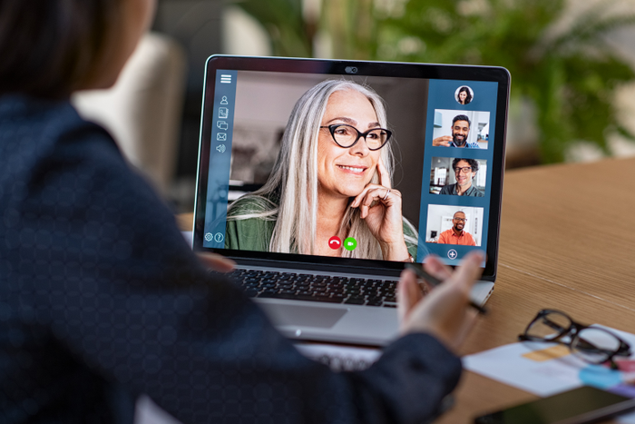 Multiethnic group having discussion in video call. A older woman appears on the laptop screen. 