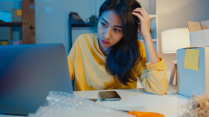 Young Asia businesswoman look around room full of product stuff and parcel box feel stress and upset with bad sell in home office at night.