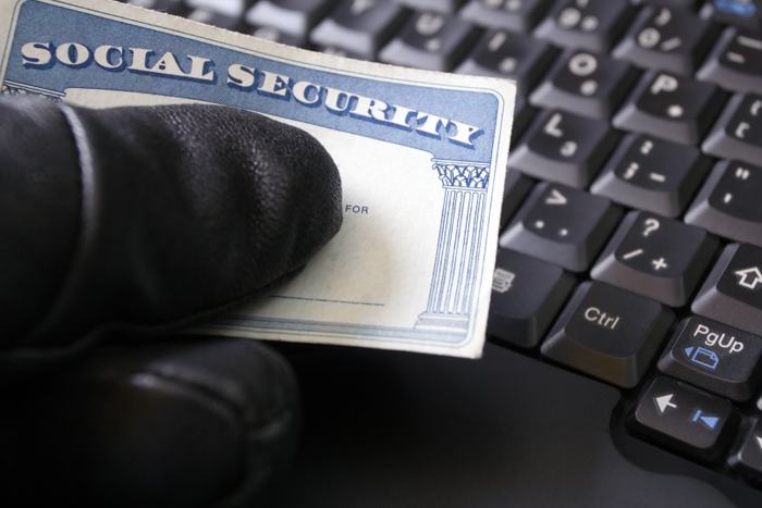 Man's hand holding Social Security card. Computer theft on laptop.