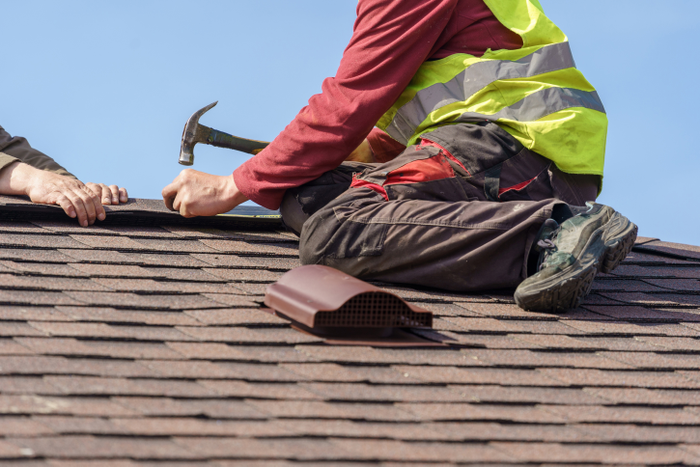 Two skilled roofer in special work wear with helmet in hands installing asphalt shingle or roof tile on top of new house