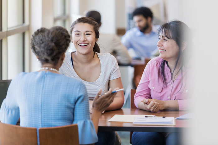 Smiling female college student discusses loan application process with loan officer. The student's mother is sitting next to her.